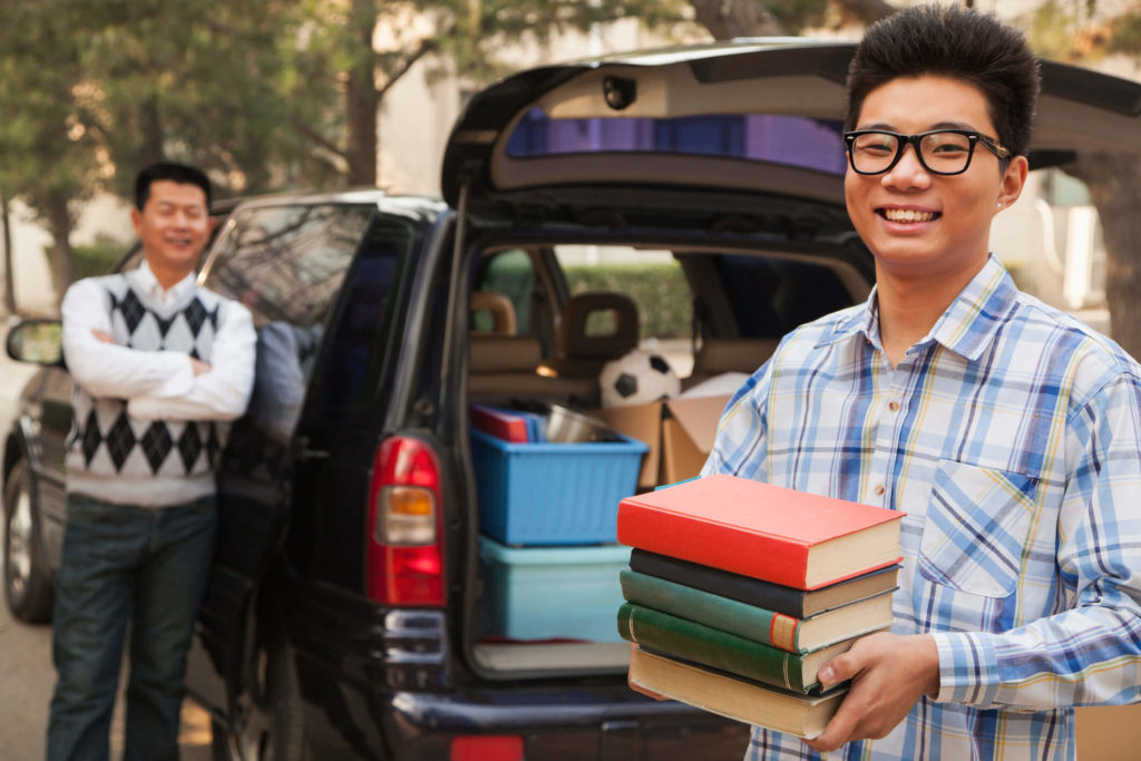 Student holds stack of books while moving into residence