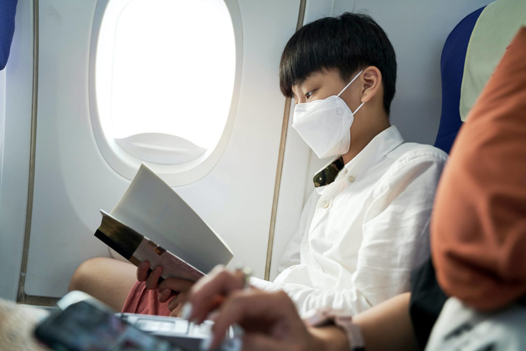 Young student wearing mask and reading on plane